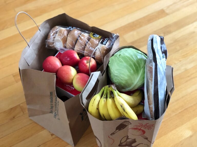 Paper grocery bags filled with apples, bananas, cabbage, bread and other food.