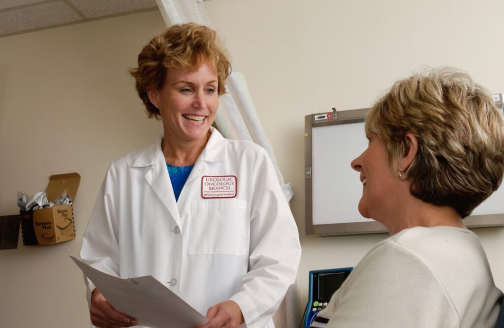A clinician holding papers while speaking with a seated patient.