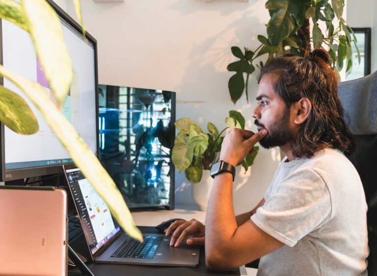 A man reviewing a computer screen at a desk with a laptop.