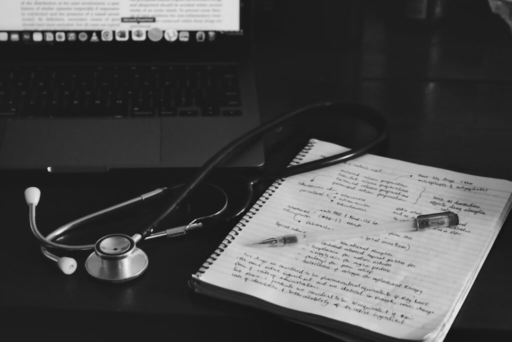 A stethoscope beside handwritten notes and a laptop