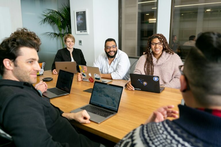 Colleagues talking around a meeting table with open laptops