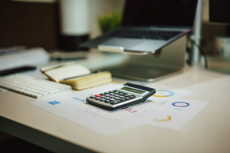 Calculator on printed charts beside a notebook and laptop.