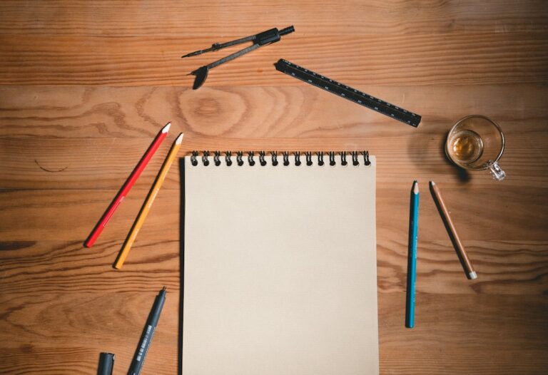 Blank sketchbook surrounded by pencils, a ruler, and a drawing compass.