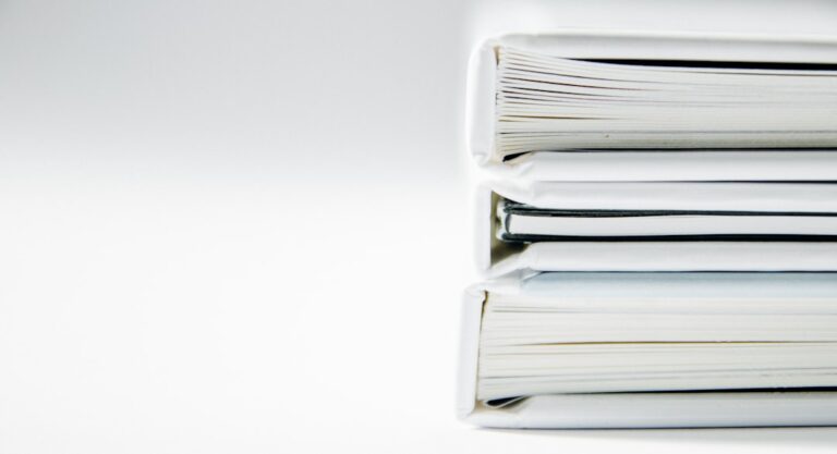 Three white document binders stacked on a light surface.