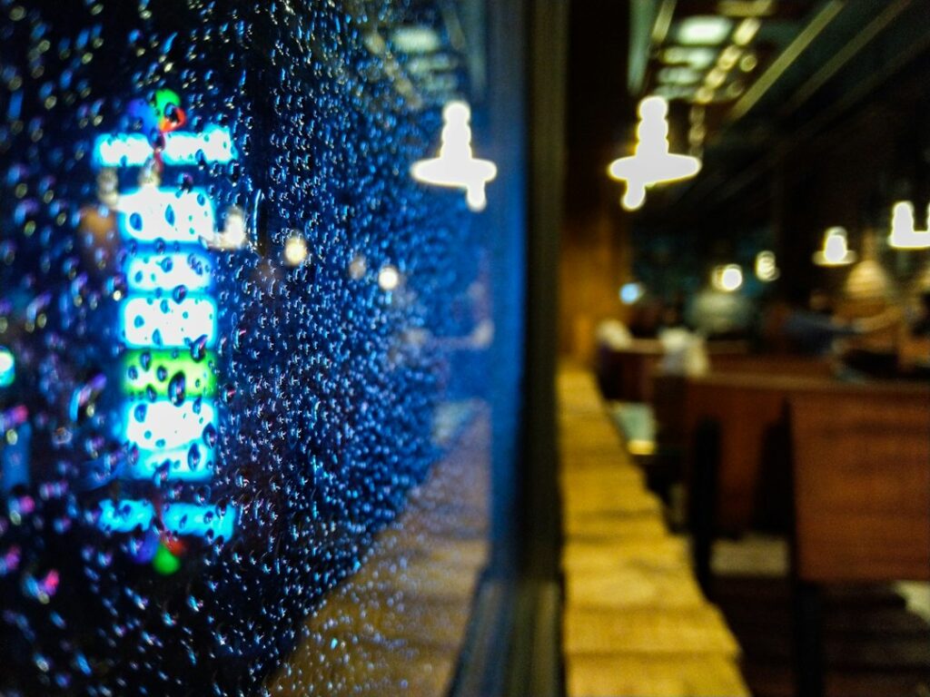 Raindrops on a window beside a softly blurred cafe interior.