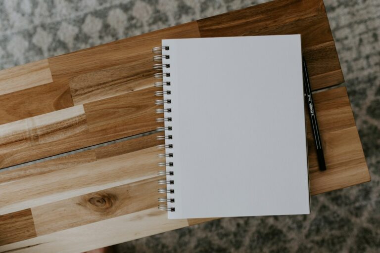 A blank spiral notebook and a pencil on a wooden table.