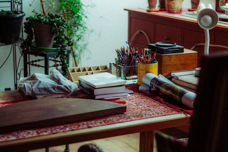 Books, pencils, brushes and scissors arranged on an artist's desk.