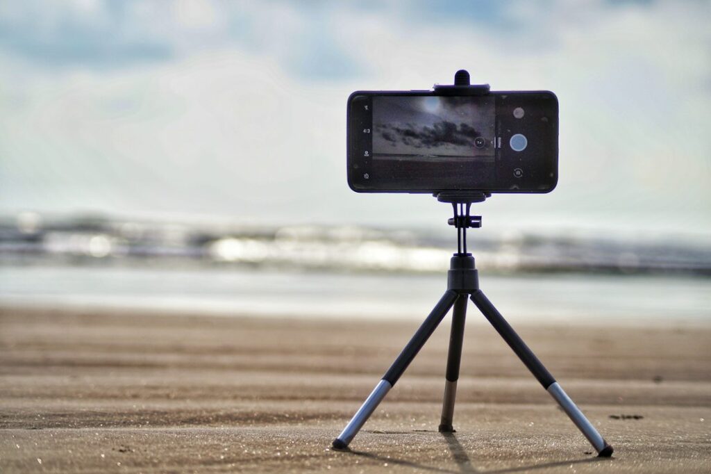 A smartphone mounted on a small tripod at the beach.