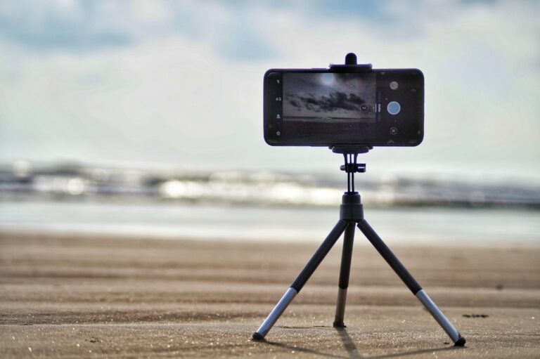 A smartphone mounted on a small tripod at the beach.