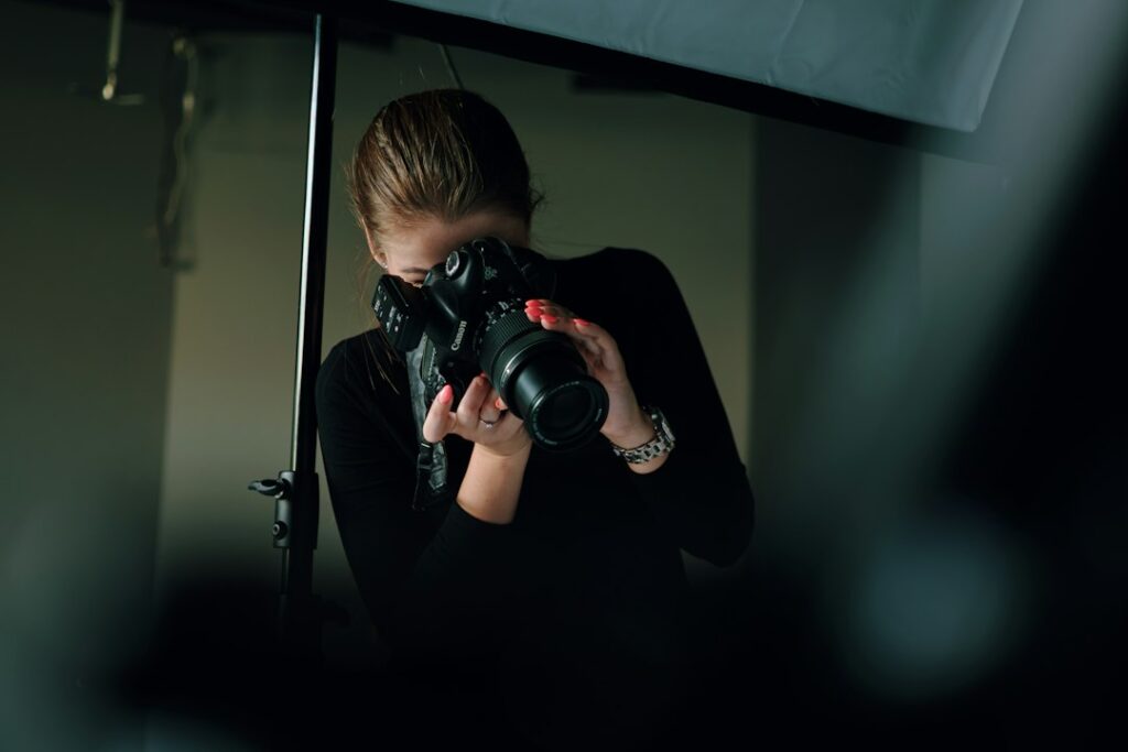 A photographer holding a camera beneath studio lighting.