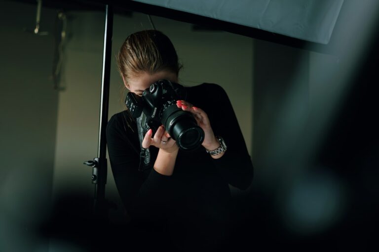 A photographer holding a camera beneath studio lighting.