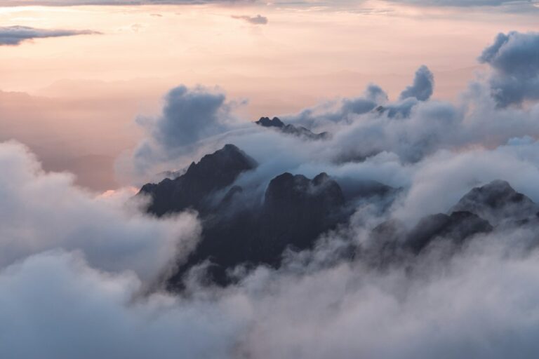 Clouds surrounding mountain peaks beneath a pale sky.