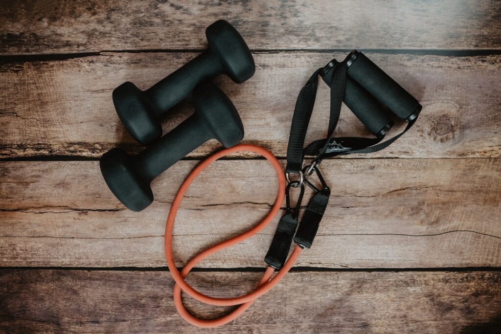 Dumbbells and a resistance tube arranged on a wooden surface