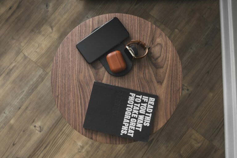 Smartphone, watch, earbud case and photography book on a round wooden table