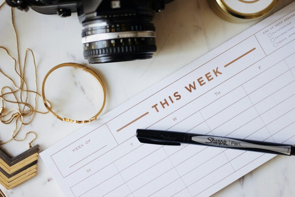 Weekly paper planner with a pen beside a camera and jewelry