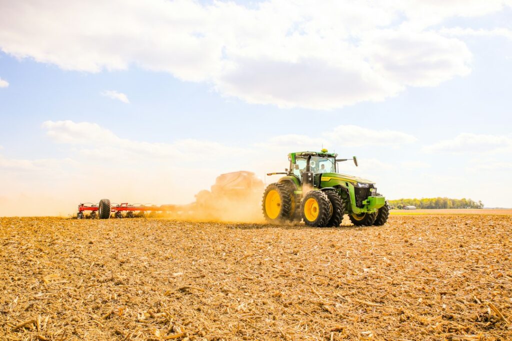 A tractor working across an open field with equipment behind it.