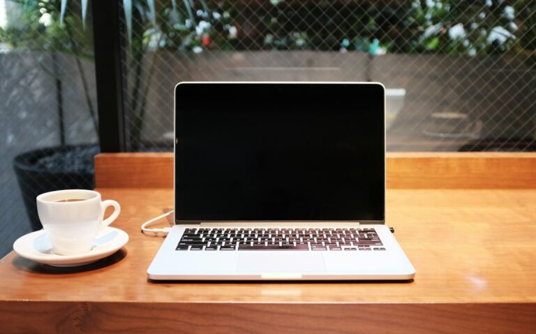 Open laptop and a white cup on a wooden table.