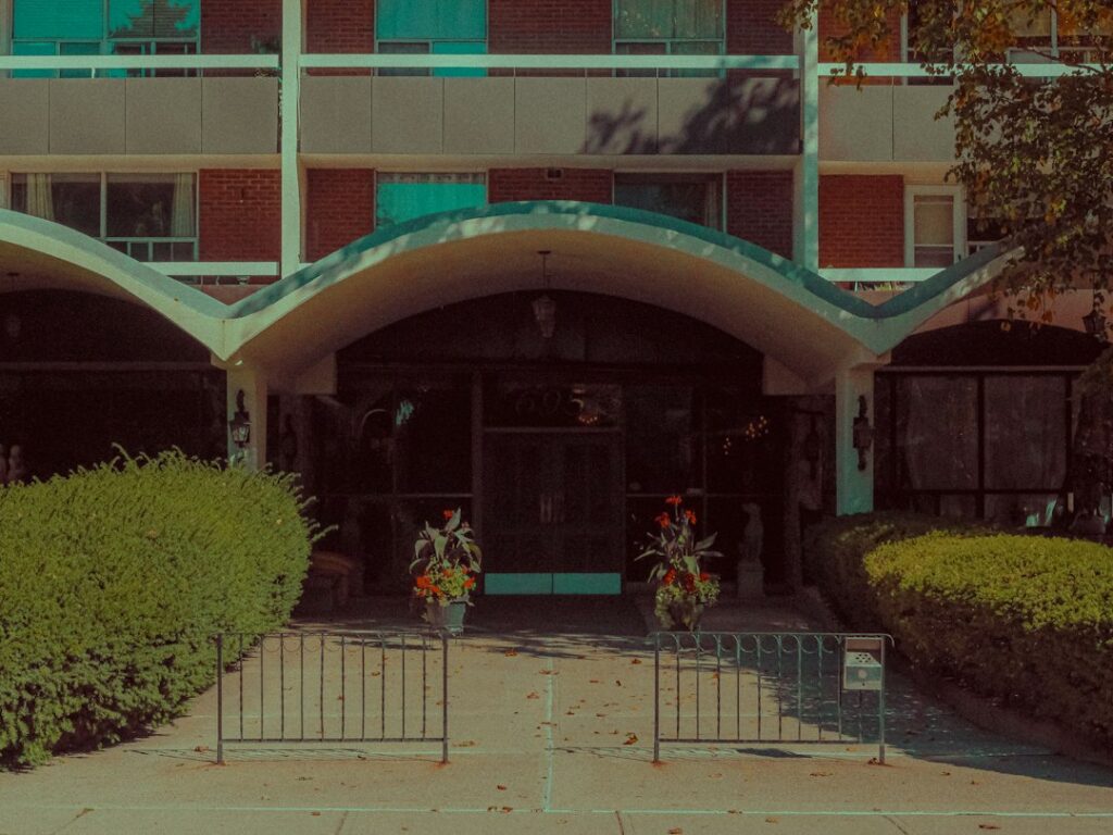 Covered entrance to a brick building, with shrubs and flower planters.