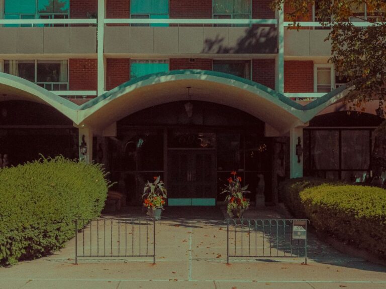 Covered entrance to a brick building, with shrubs and flower planters.