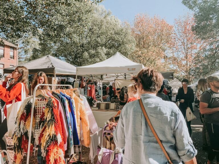 Shoppers browsing clothing racks at an outdoor market.