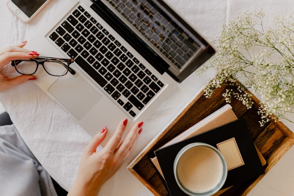 Overhead view of hands beside a laptop, glasses, notebooks, and a cup of coffee.