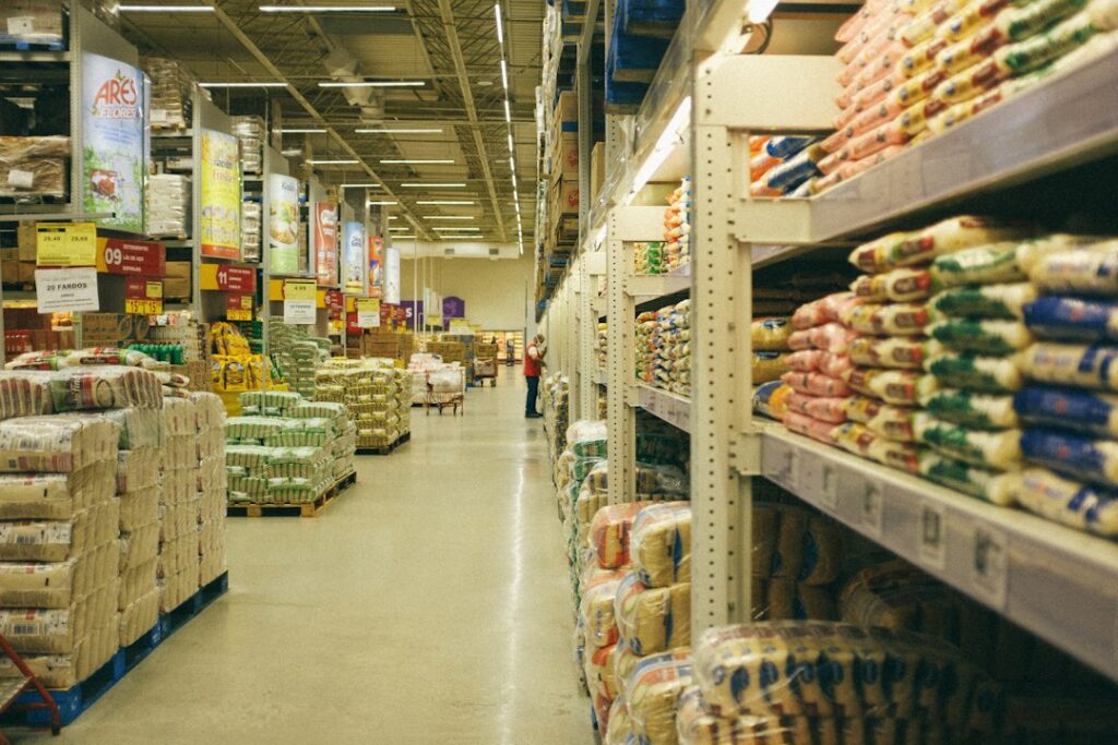 Store aisle with packaged goods stacked on shelves and pallets.