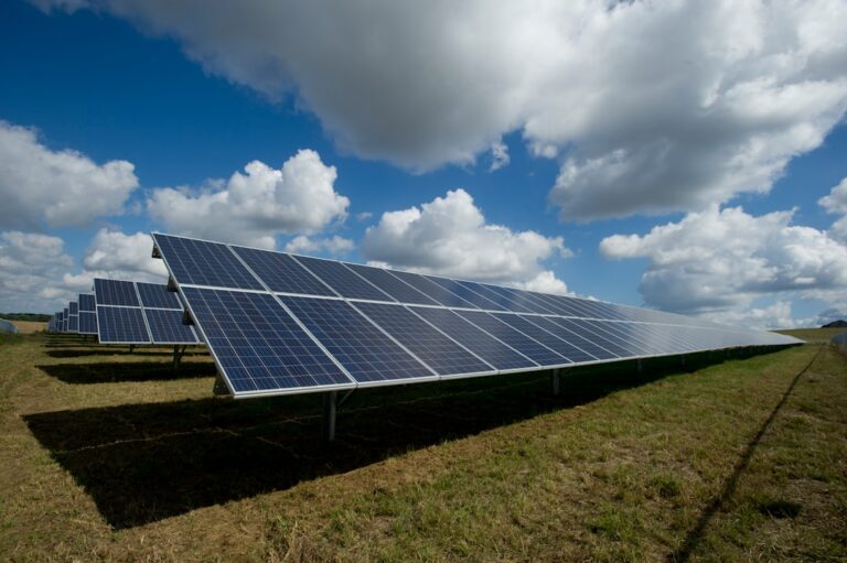 Rows of solar panels in a grassy field beneath a partly cloudy sky.