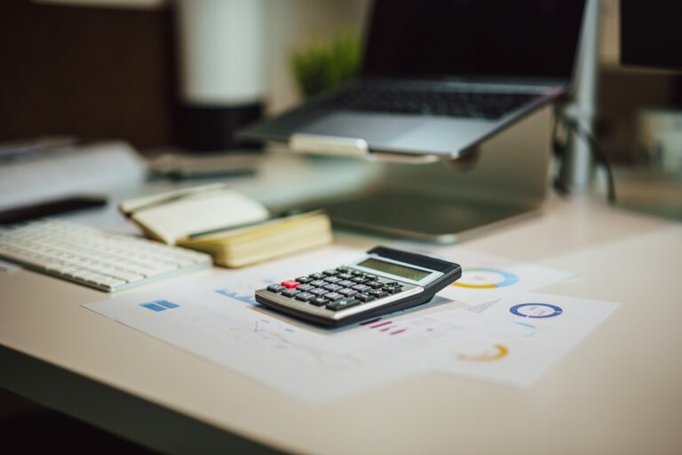 A calculator resting on printed charts beside a laptop and notebook.
