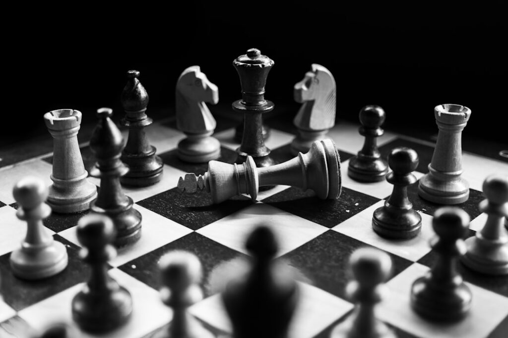 Black-and-white photograph of chess pieces on a board, with one king lying on its side.
