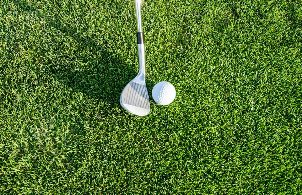 A golf iron beside a white golf ball on short green grass