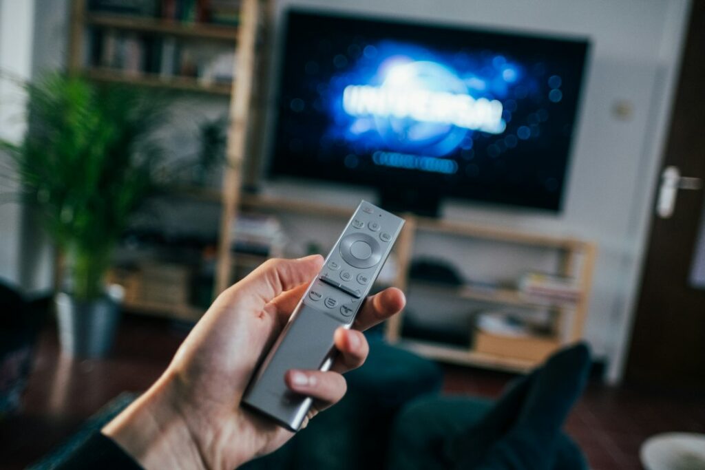 Hand holding a television remote in front of a living-room television