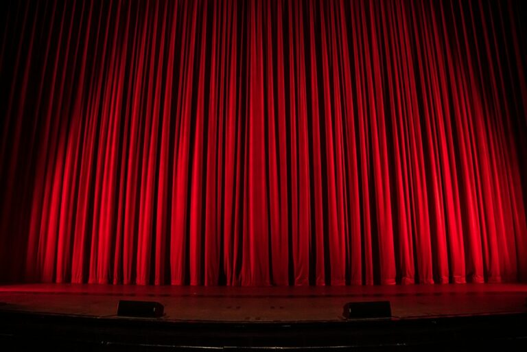 Closed red theatre curtains above an empty stage