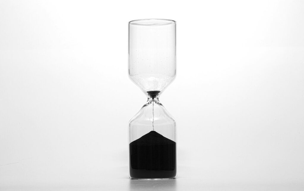 A clear glass hourglass with dark sand on a light background.