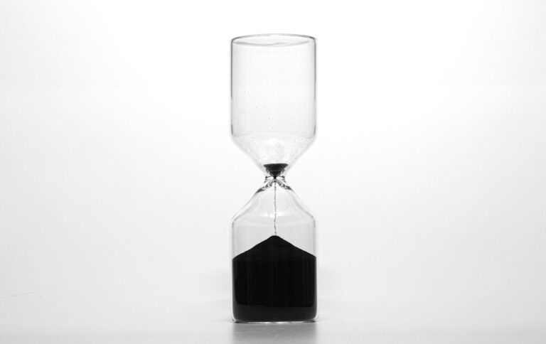 A clear glass hourglass with dark sand on a light background.