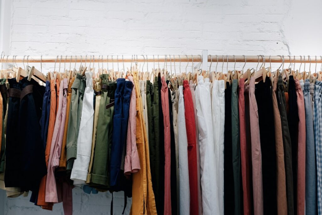 Trousers in many colors hanging from wooden hangers against a white brick wall.