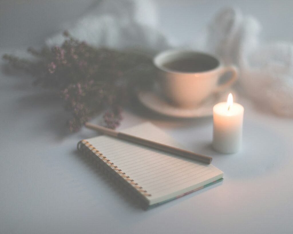 A lined notebook and pencil beside a cup and a lit candle