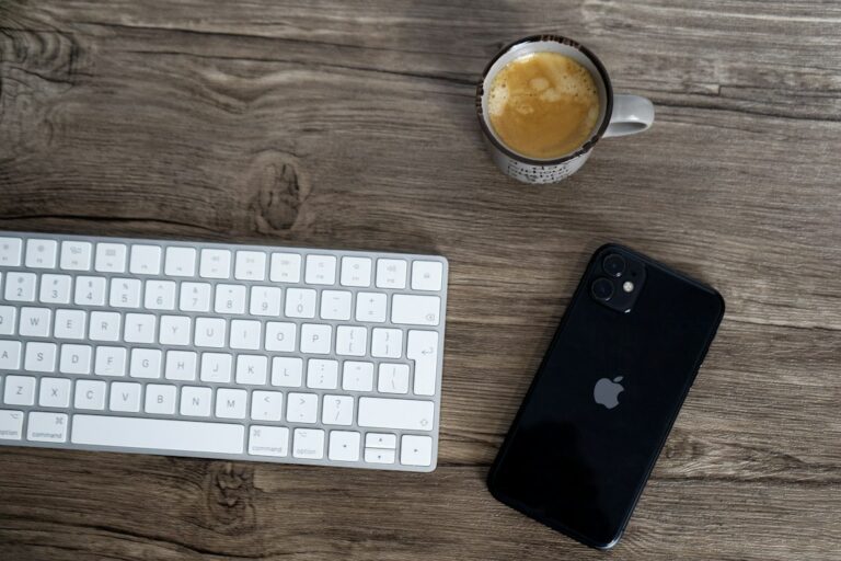 A smartphone, keyboard and cup of coffee on a wooden desk.
