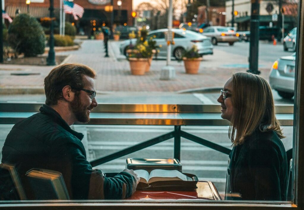 Two people having a conversation beside a cafe window.