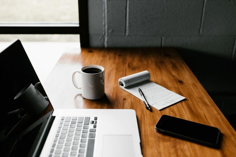 Laptop, coffee cup, notepad, pen and phone on a wooden table