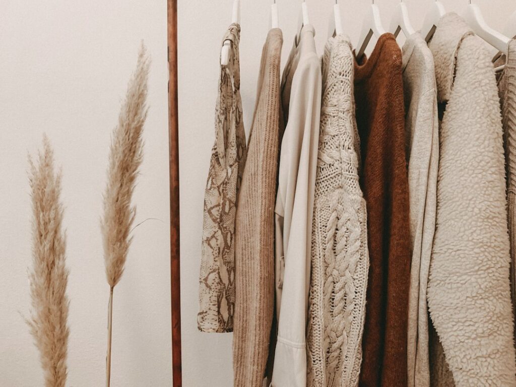 Neutral-colored garments and knitwear hanging beside dried grasses