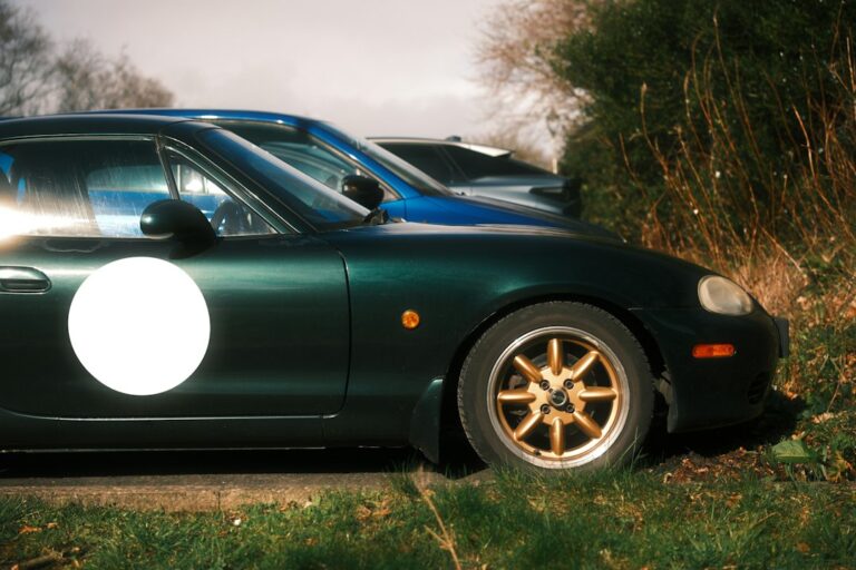 Front and side of a dark green convertible parked beside other cars.