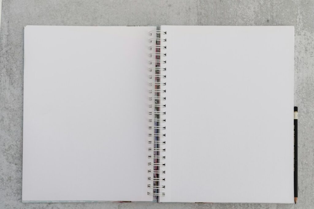 An open blank spiral notebook with a pencil on a gray surface.