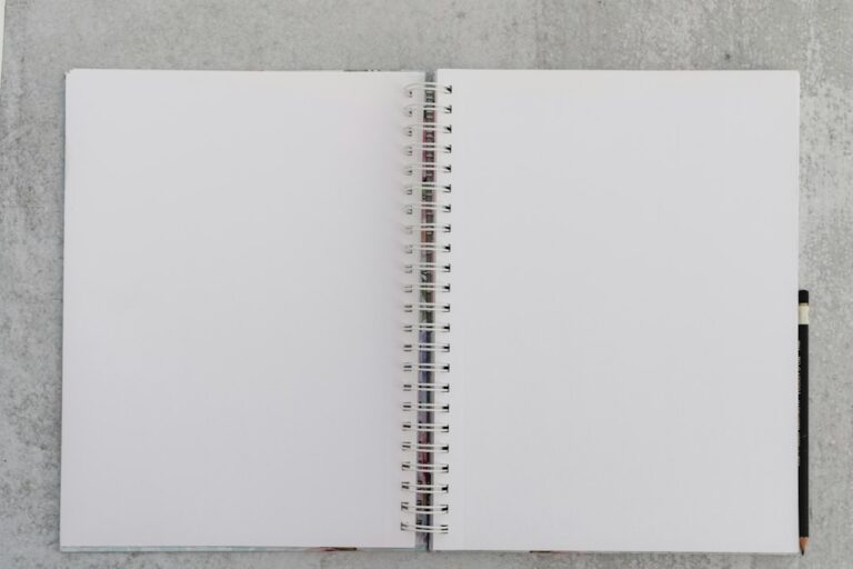 An open blank spiral notebook with a pencil on a gray surface.
