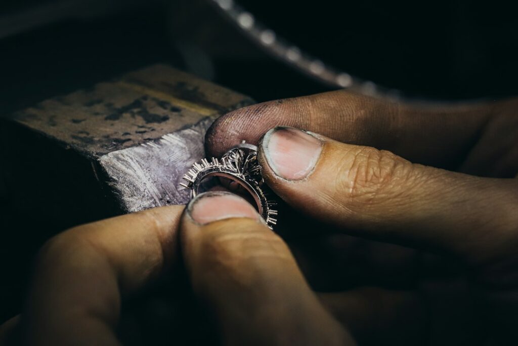 Close-up of a craftsperson's fingers holding an unfinished ring beside a jewelry workbench.