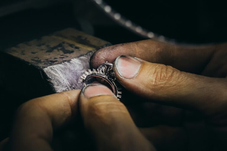 Close-up of a craftsperson's fingers holding an unfinished ring beside a jewelry workbench.