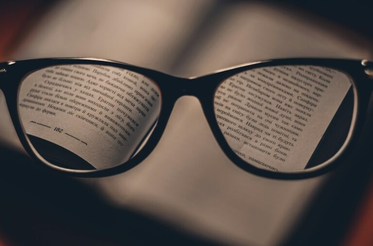 Reading glasses held above an open book, with printed text visible through the lenses.
