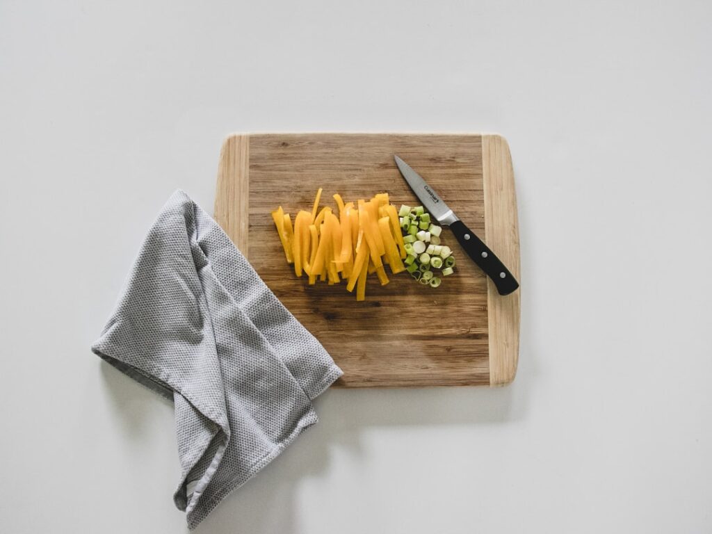 Sliced yellow pepper and spring onion on a wooden cutting board beside a kitchen knife