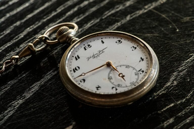 A pocket watch with a white dial resting on dark wood.
