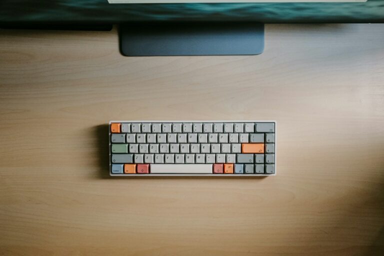 Compact keyboard beneath a computer monitor on a wooden desk.