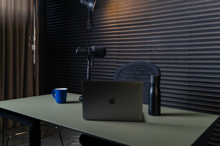 Microphone and laptop on a desk with a mug and water bottle